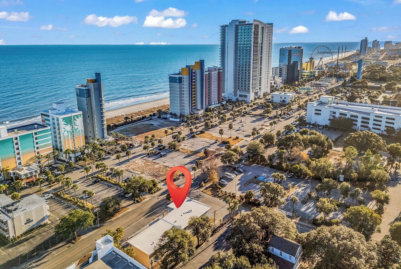 Aerial view of a beachfront city with high-rise buildings, sandy shore, and a red map pin marker.