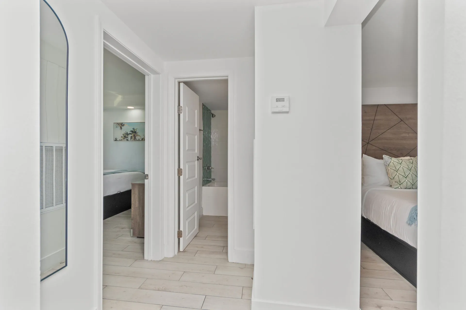 Bright hallway with open doors to two bedrooms and a bathroom, white walls and light wood floors.