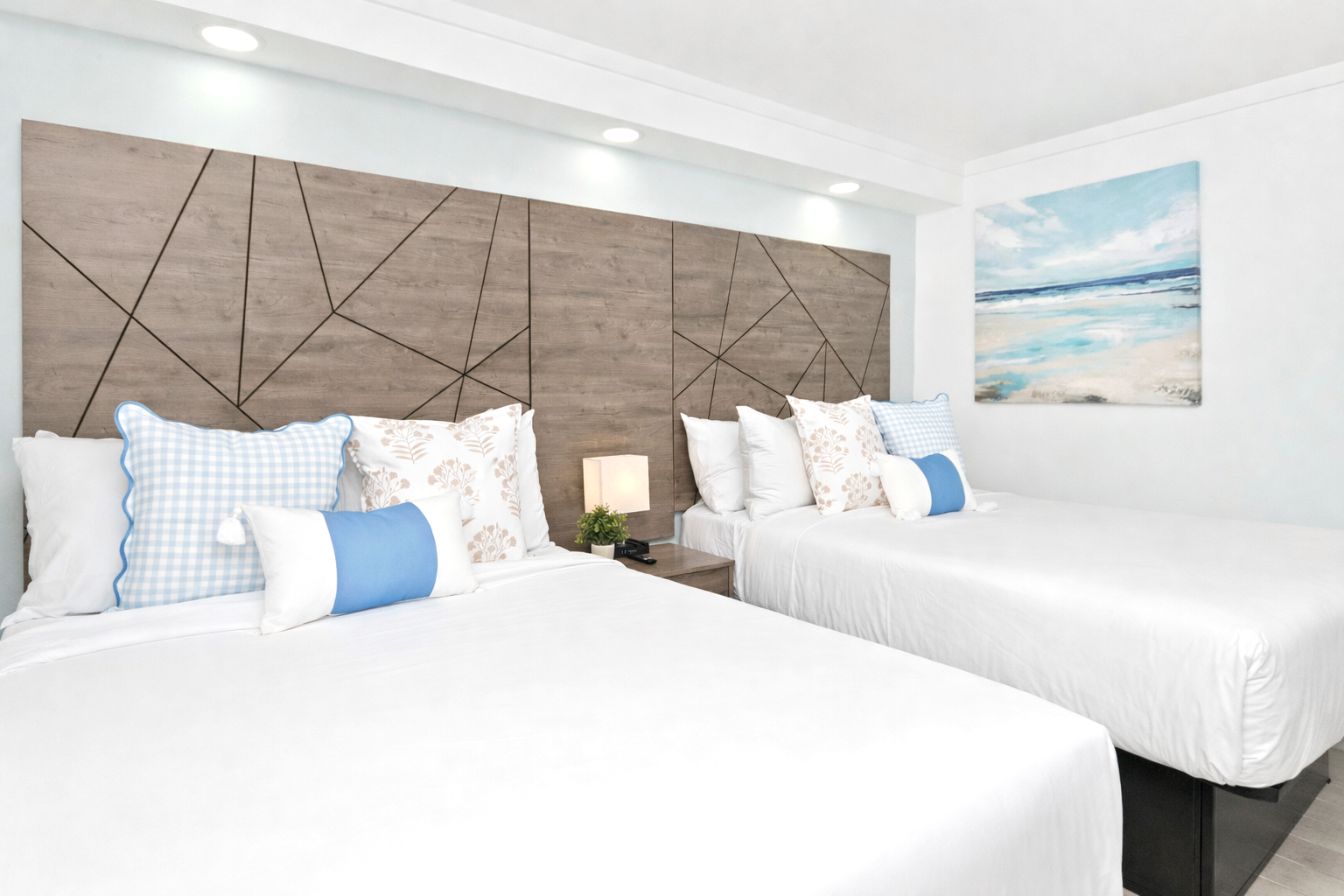 Bright hotel room with two white beds, blue accent pillows, and abstract wall art