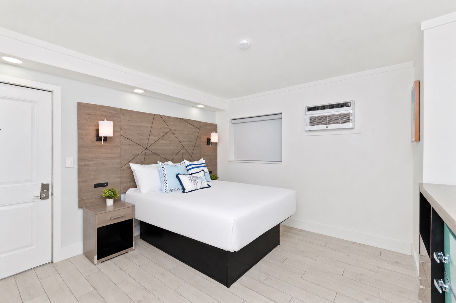 Bright white bedroom with a bed, wood headboard, nightstand, and window blinds
