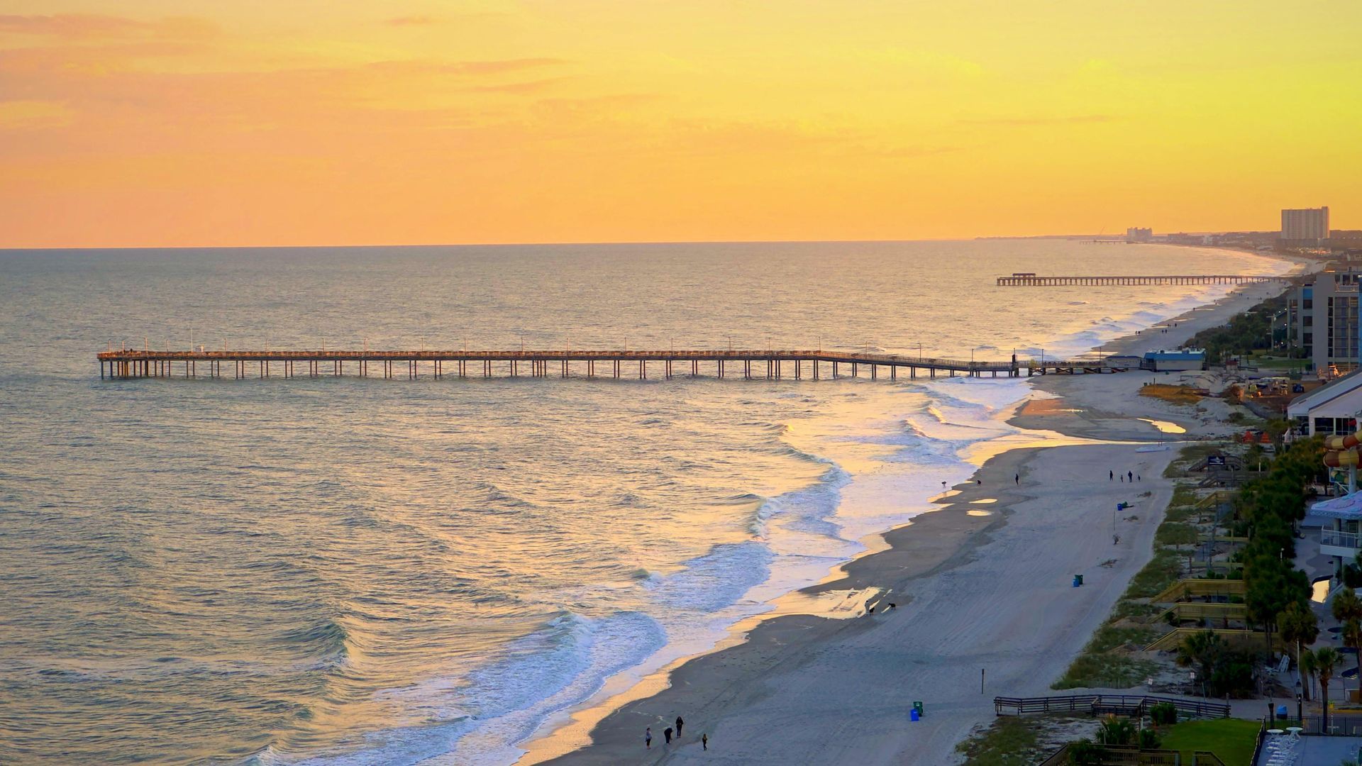 Sunset over a beach with a long pier and gentle waves along the shore