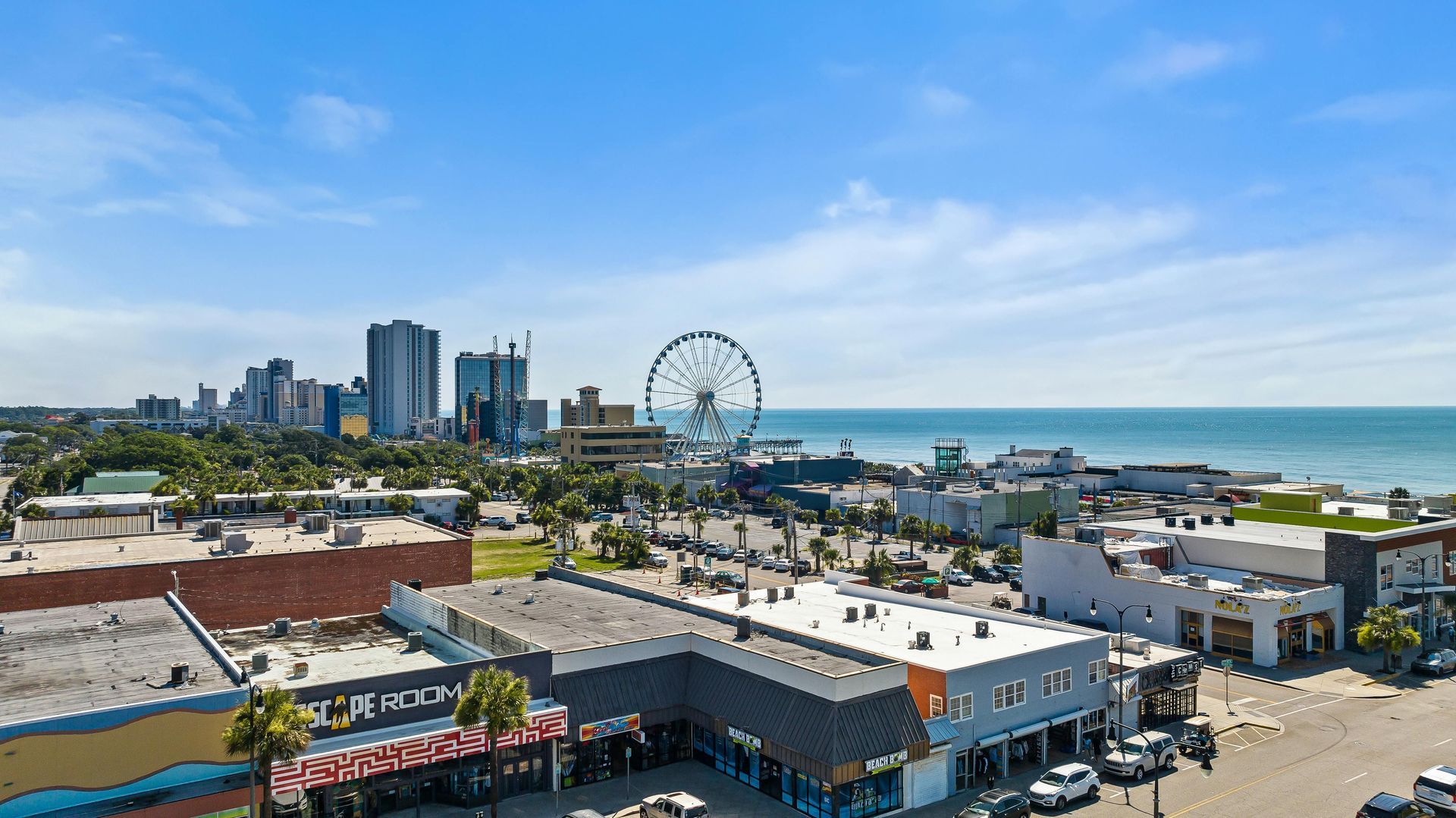Coastal city skyline with a Ferris wheel, low-rise buildings, and ocean under a clear blue sky