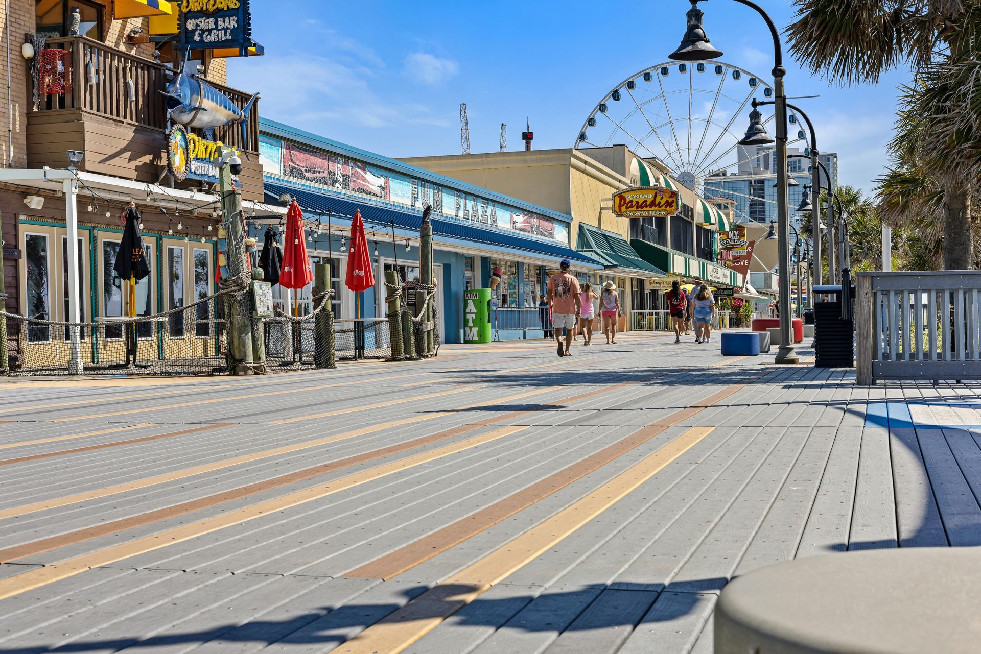 Empty seaside boardwalk lined with closed cafés and umbrellas on a sunny day
