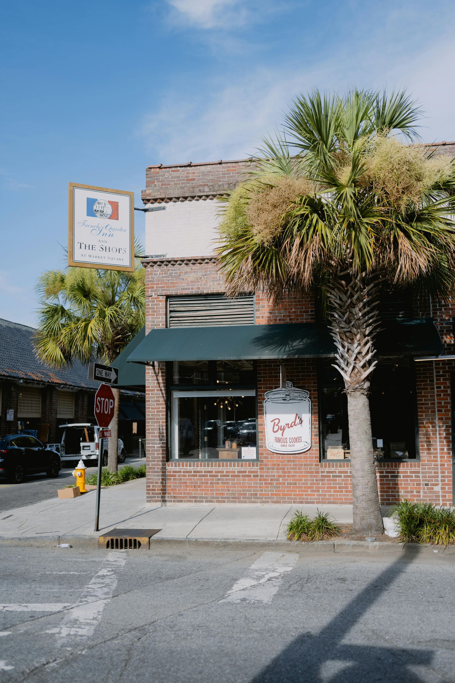 Storefront with green awning, palm tree, and brick facade on a sunny street.