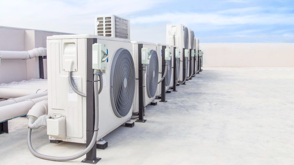 Row of white air conditioning units on a rooftop against a blue sky.