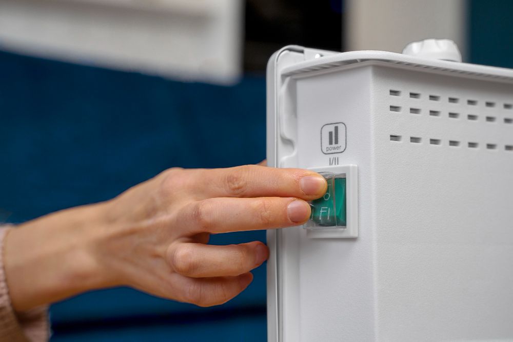 Hand turning on a white space heater with a green power switch.