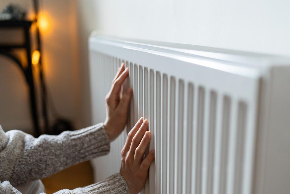 Hands warming on a white radiator in front of a white wall.