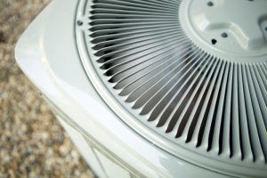 Close-up of a white air conditioning unit's fan blades, set on a gravel surface.