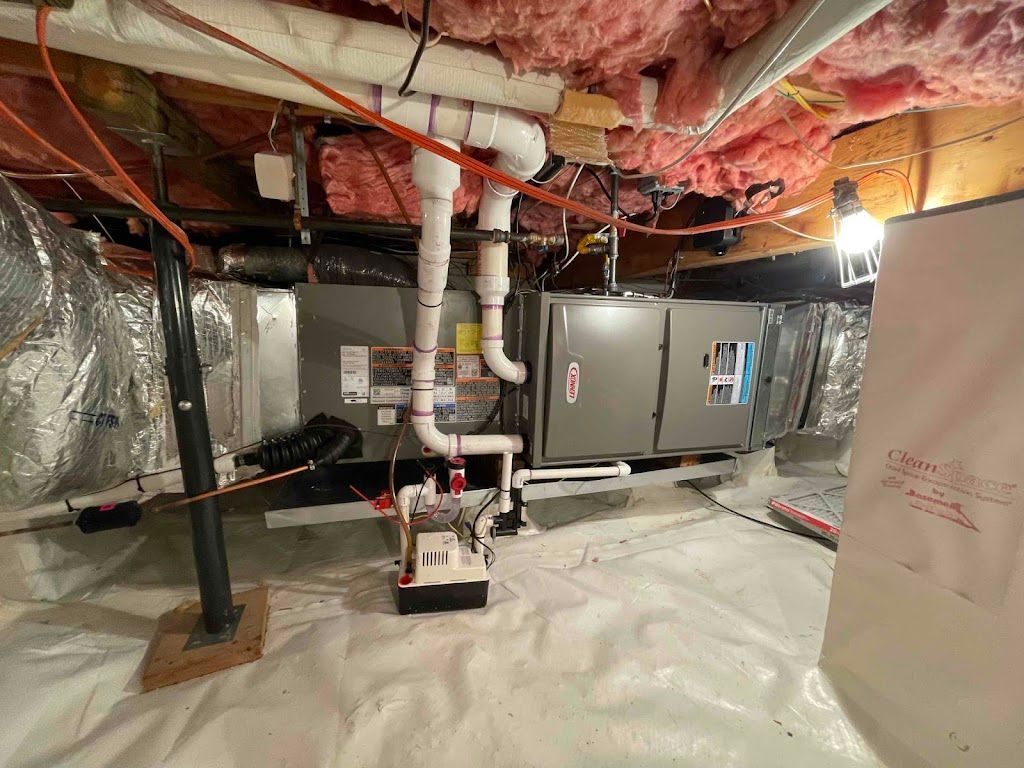 HVAC unit in a crawl space with white flooring, pink insulation, and pipes.
