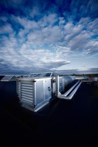 HVAC system on a dark roof against a cloudy blue sky.
