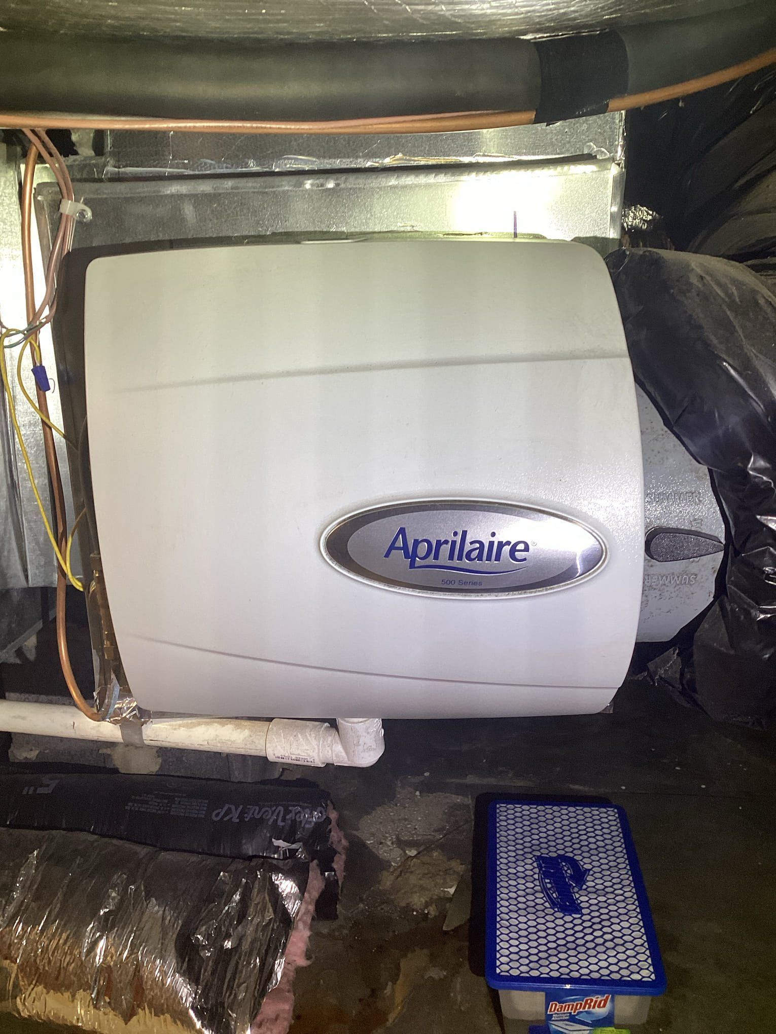 HVAC technician in uniform examining a furnace. He kneels, wearing gloves, in a basement.
