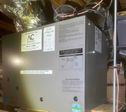 HVAC technician in blue hard hat checks air conditioning units with gauges, outdoors.