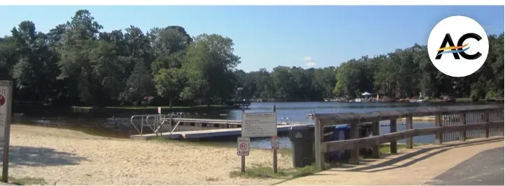 Sandy beach area with lake, dock, and wooded backdrop.