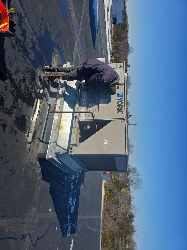 Person working on a rooftop air conditioning unit, on a sunny day.