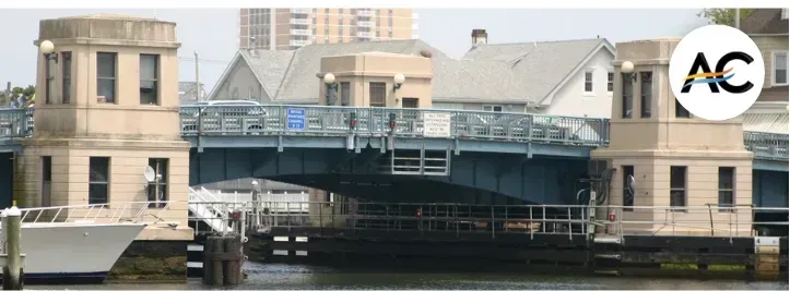 Drawbridge over a waterway, with stone control towers and a building in the background.