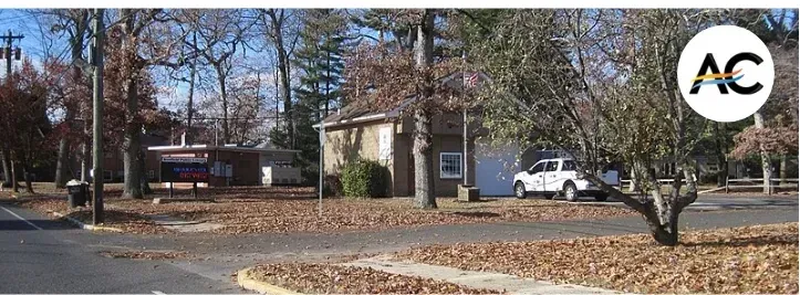 A fall landscape with trees, a building, a white car, and a logo in the top right.