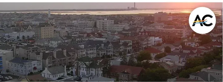 Aerial view of a city at sunset. Buildings are visible with a body of water in the background. The sky is orange.