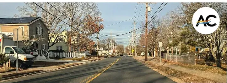 Street with houses, power lines, and a truck on the side. Clear sky.