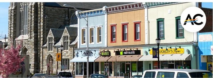 Row of storefronts on a sunny street with a church on the left.