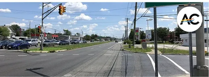 A street with cars parked on both sides, a traffic light, and cloudy blue sky.