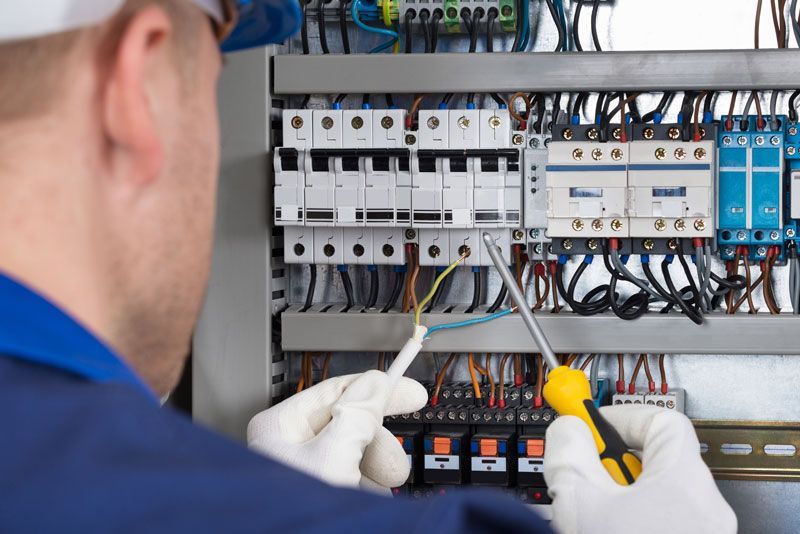 An electrician is working on a circuit board with a screwdriver.