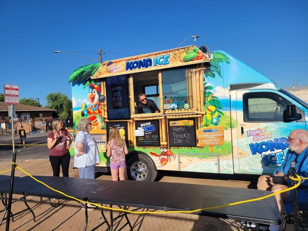 A food truck is parked on the side of the road next to a table.