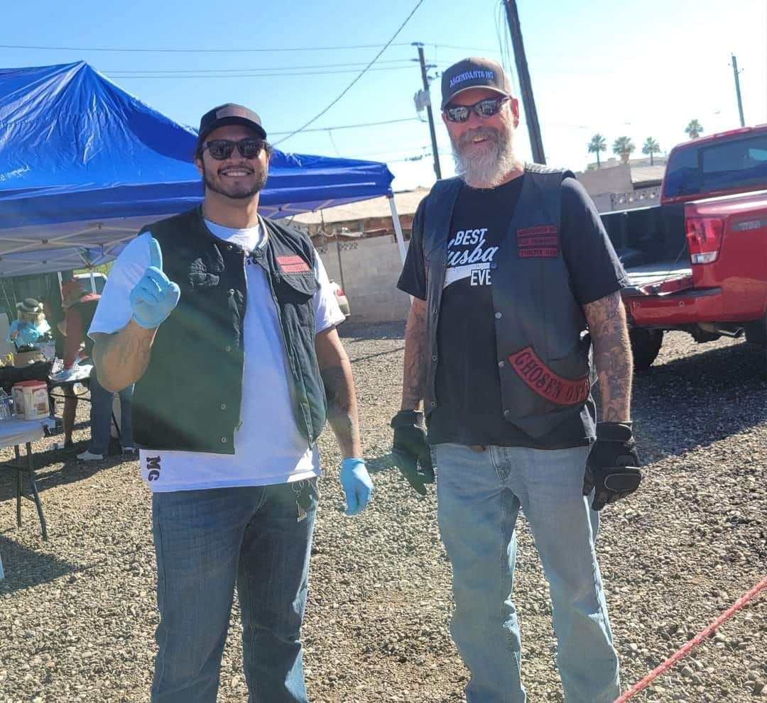 Two men are standing next to each other in a dirt field.