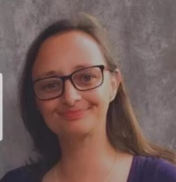 Smiling woman with glasses and long hair against a gray backdrop