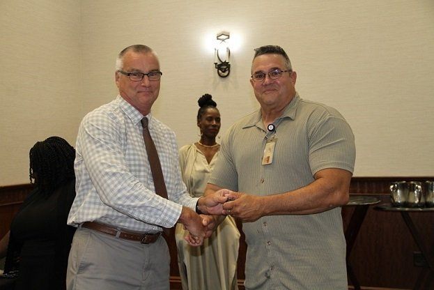 two men are shaking hands in a room with a woman in the background .