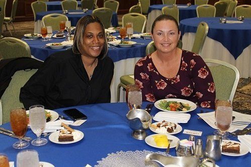 two women are sitting at a table with plates of food and glasses of water .