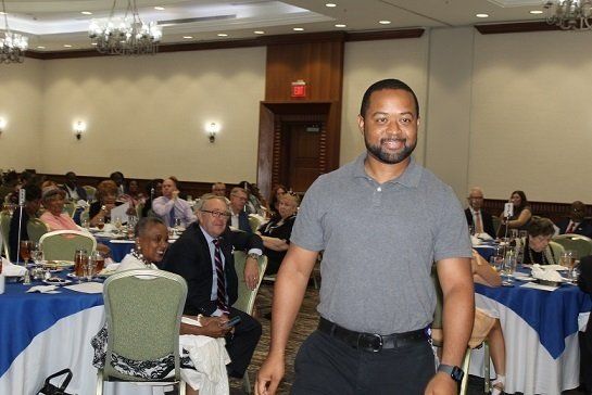 a man stands in front of a group of people sitting at tables