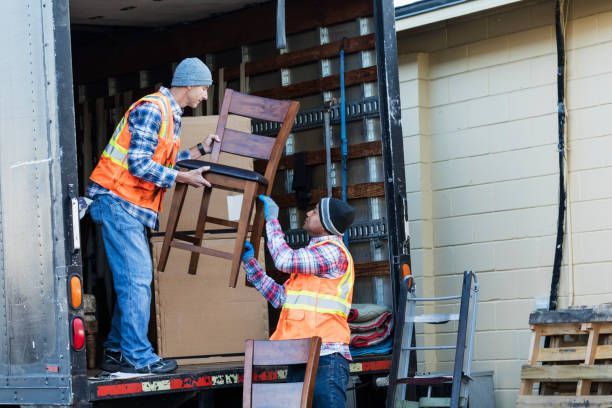 Two movers loading chairs into a truck; wearing safety vests and gloves.