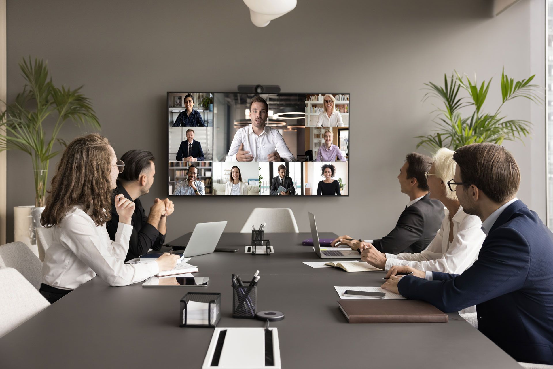 A group of people are sitting around a conference table having a video call.