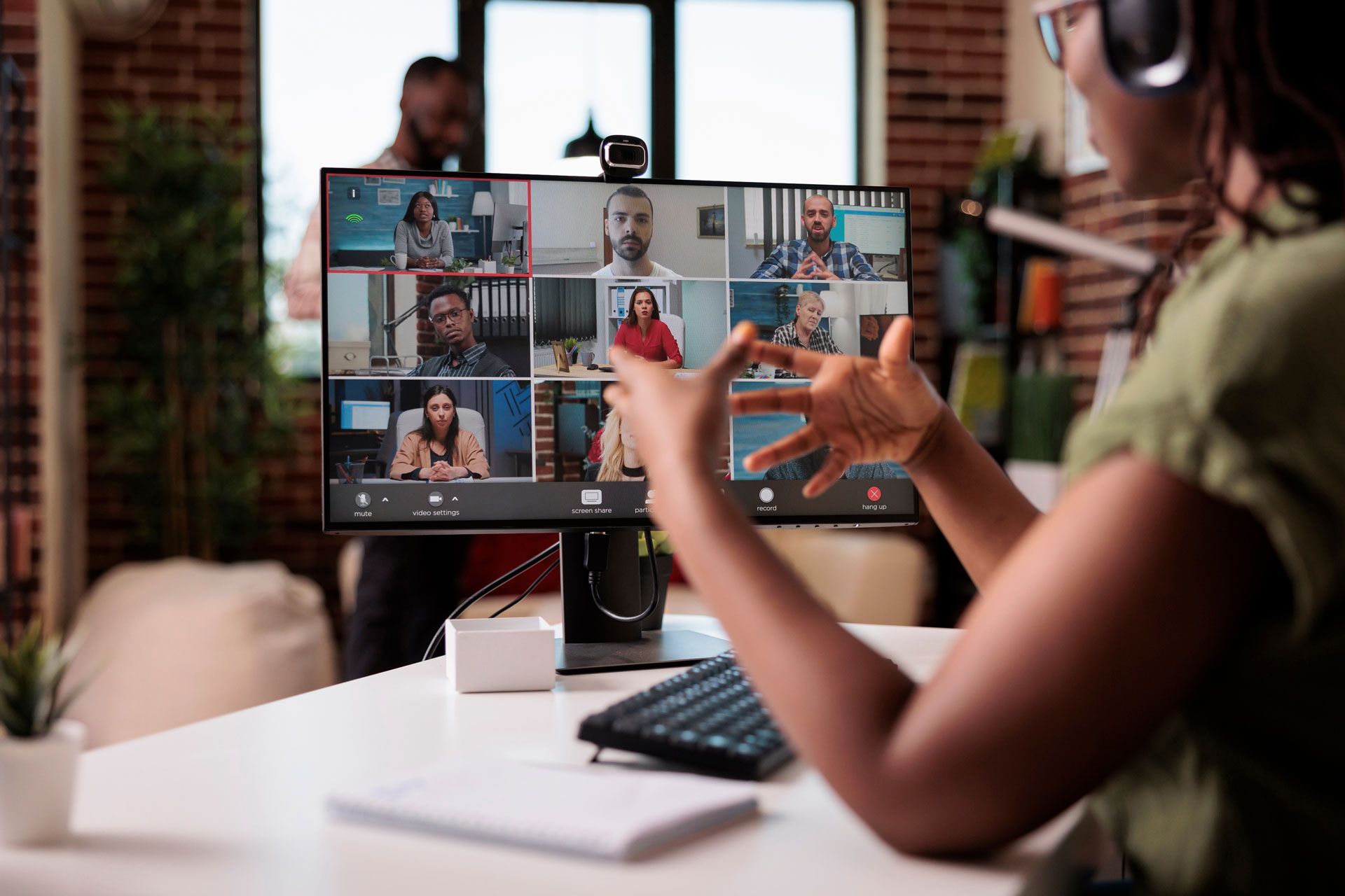 A woman is sitting at a desk using a computer to have a video call with a group of people.