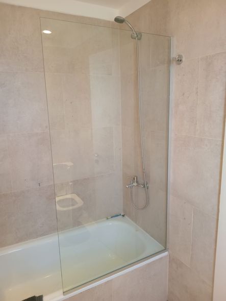 Cabina de ducha de cristal con paredes alicatadas en color beige y bañera blanca en un baño.