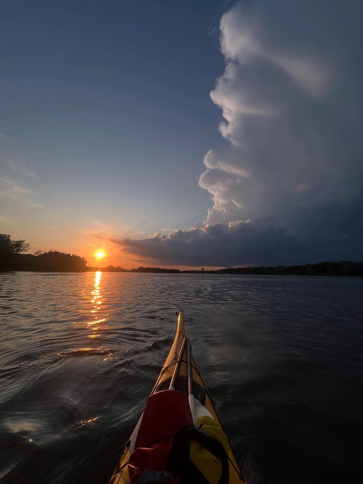 Kayak bow on calm water at sunset beside a towering storm cloud over the horizon