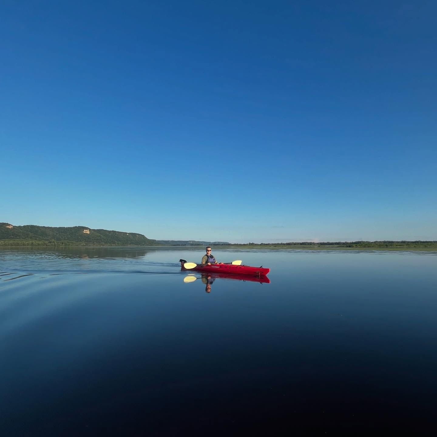 Red kayak with a paddler on a calm blue lake under a clear sky.