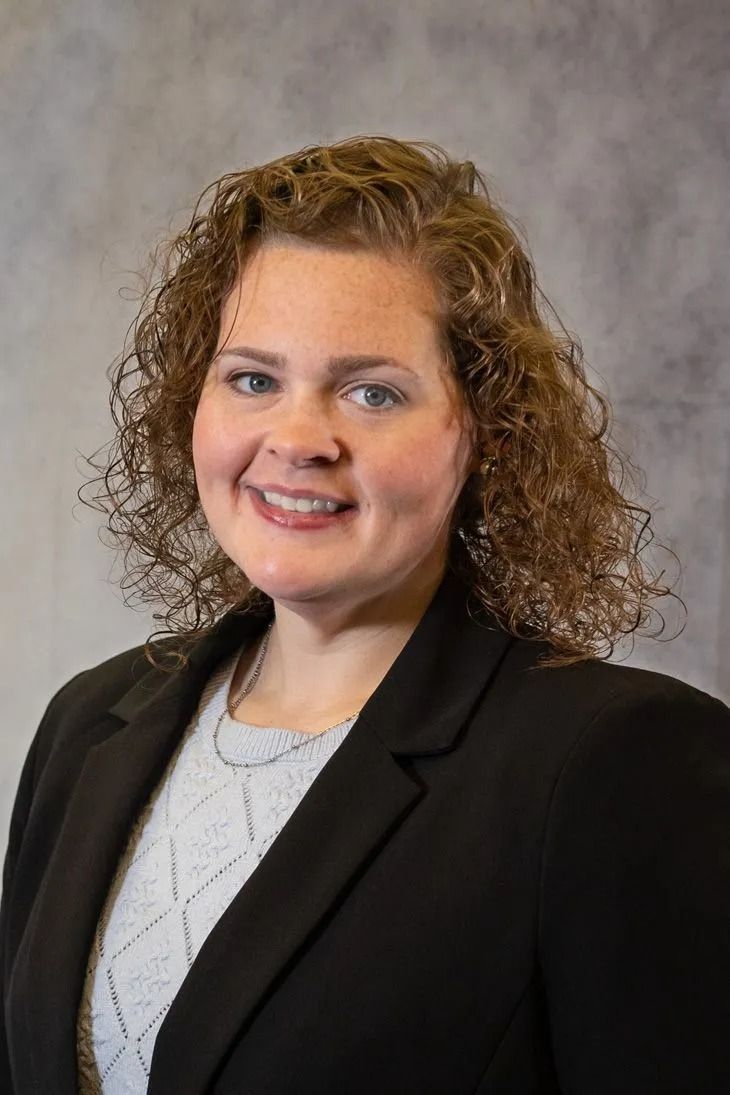 Smiling professional in a black blazer against a gray studio backdrop