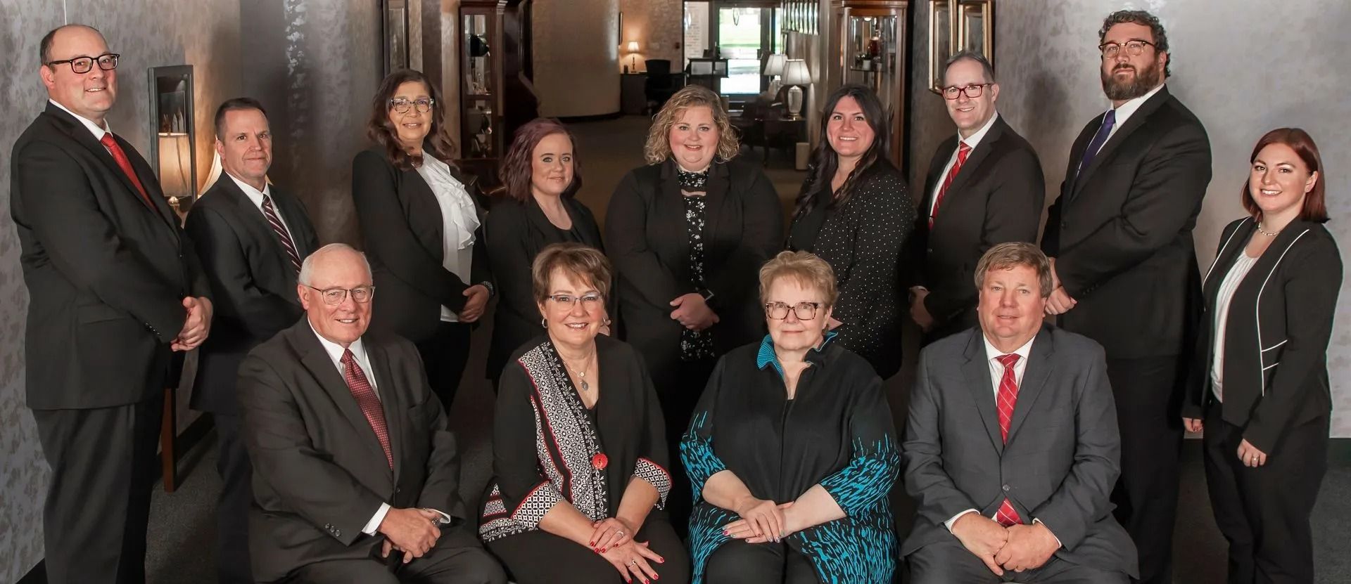 Group portrait of 11 people in formal attire standing and sitting indoors on a staircase landing
