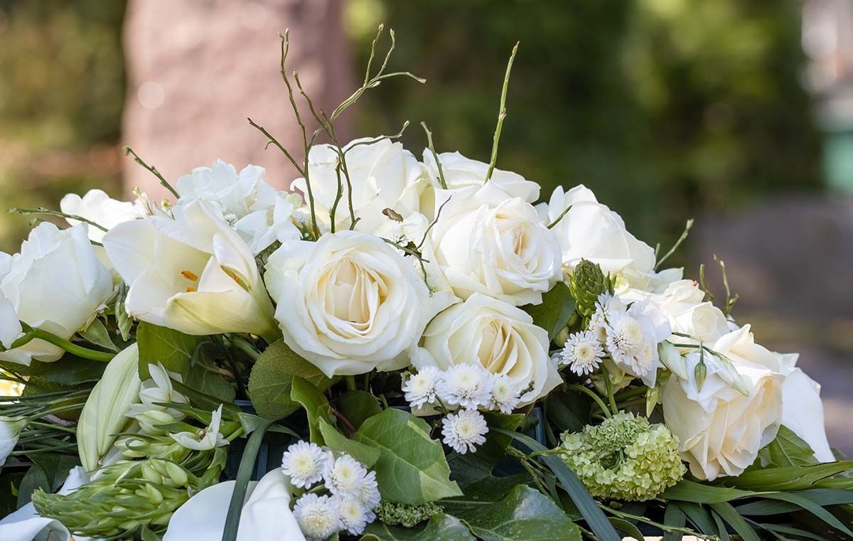 White roses and small white flowers arranged in a floral bouquet with green leaves outdoors