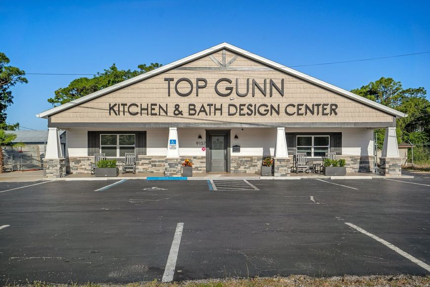 Exterior of Top Gunn Kitchen & Bath Design Center: tan building with black text, blue sky, empty parking lot.
