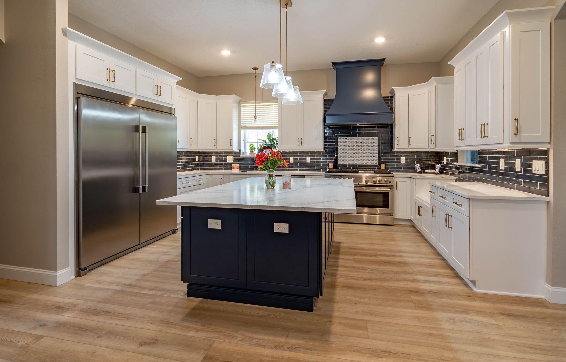 Modern kitchen with white cabinets, navy island, stainless steel appliances, and wood floors.