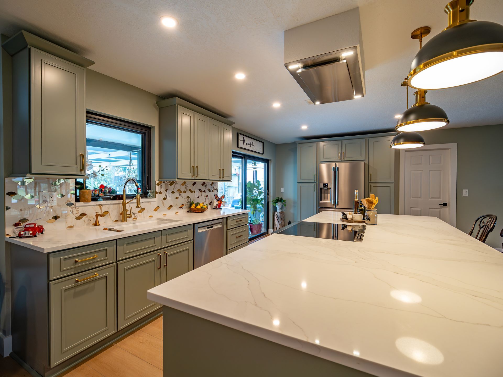 Green kitchen with white countertops, stainless steel appliances, and pendant lights.