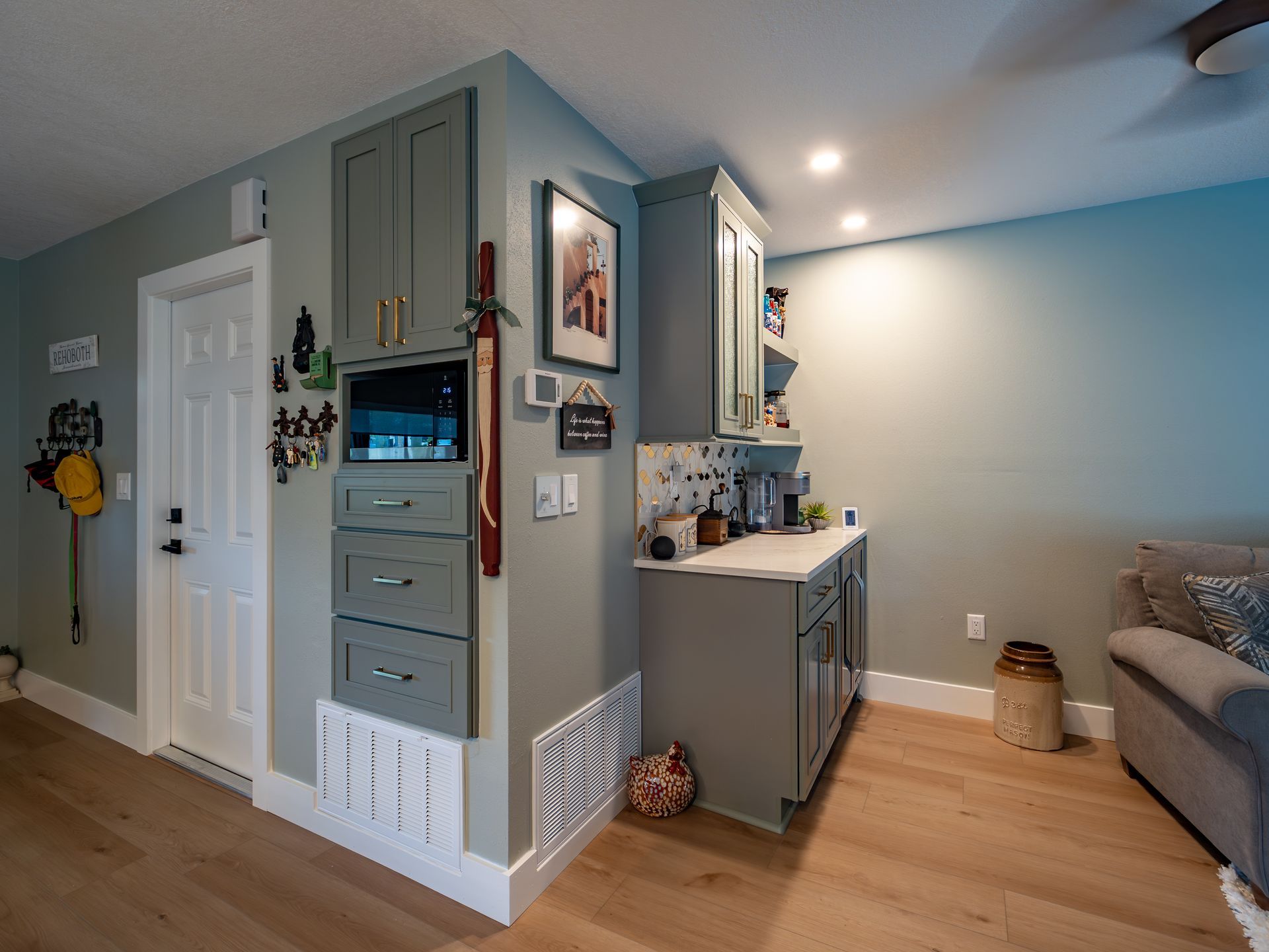 A kitchen area with gray cabinets, white door, and light wood floors.
