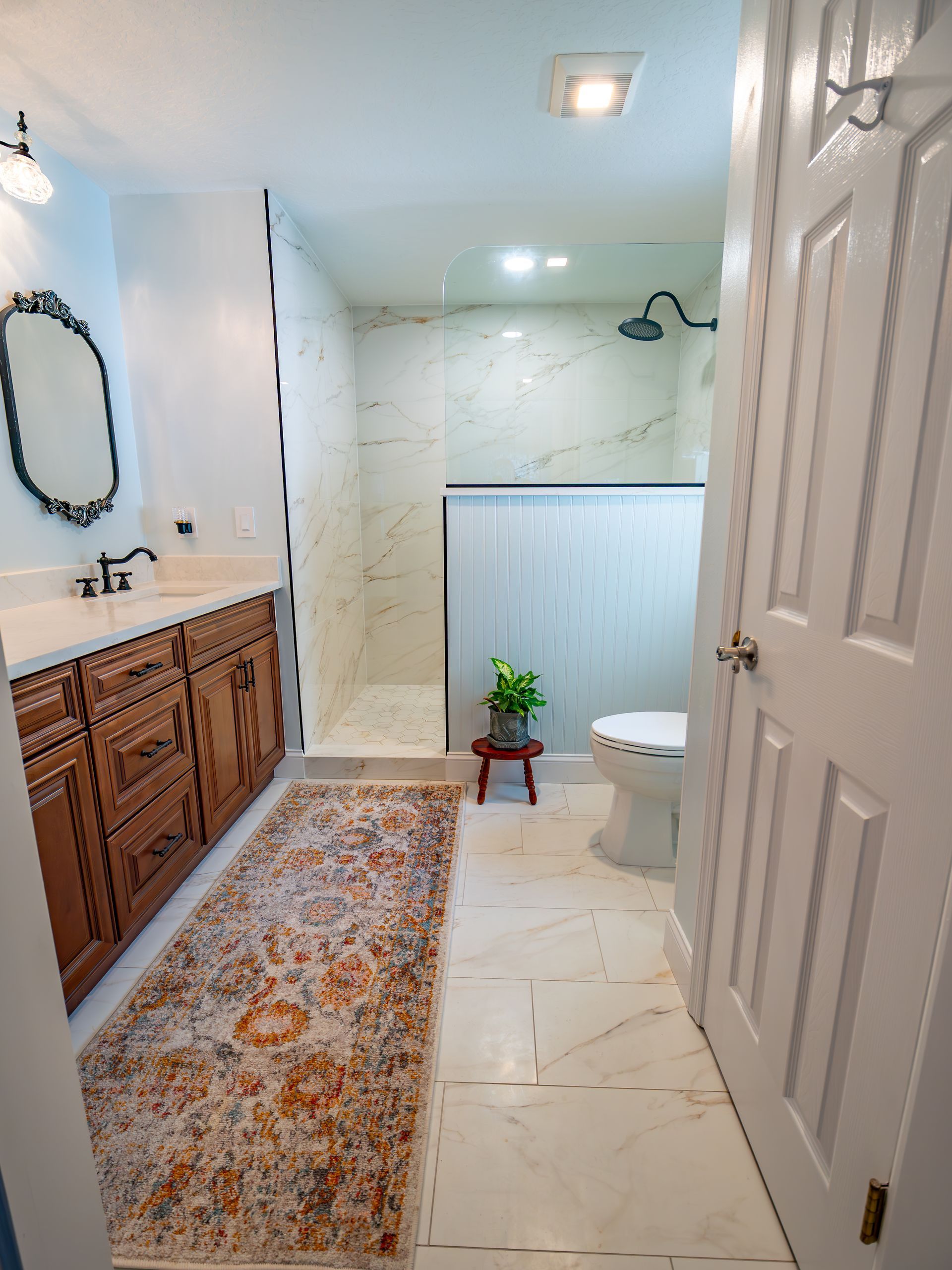 Bathroom with marble shower, vanity with mirror, and rug.