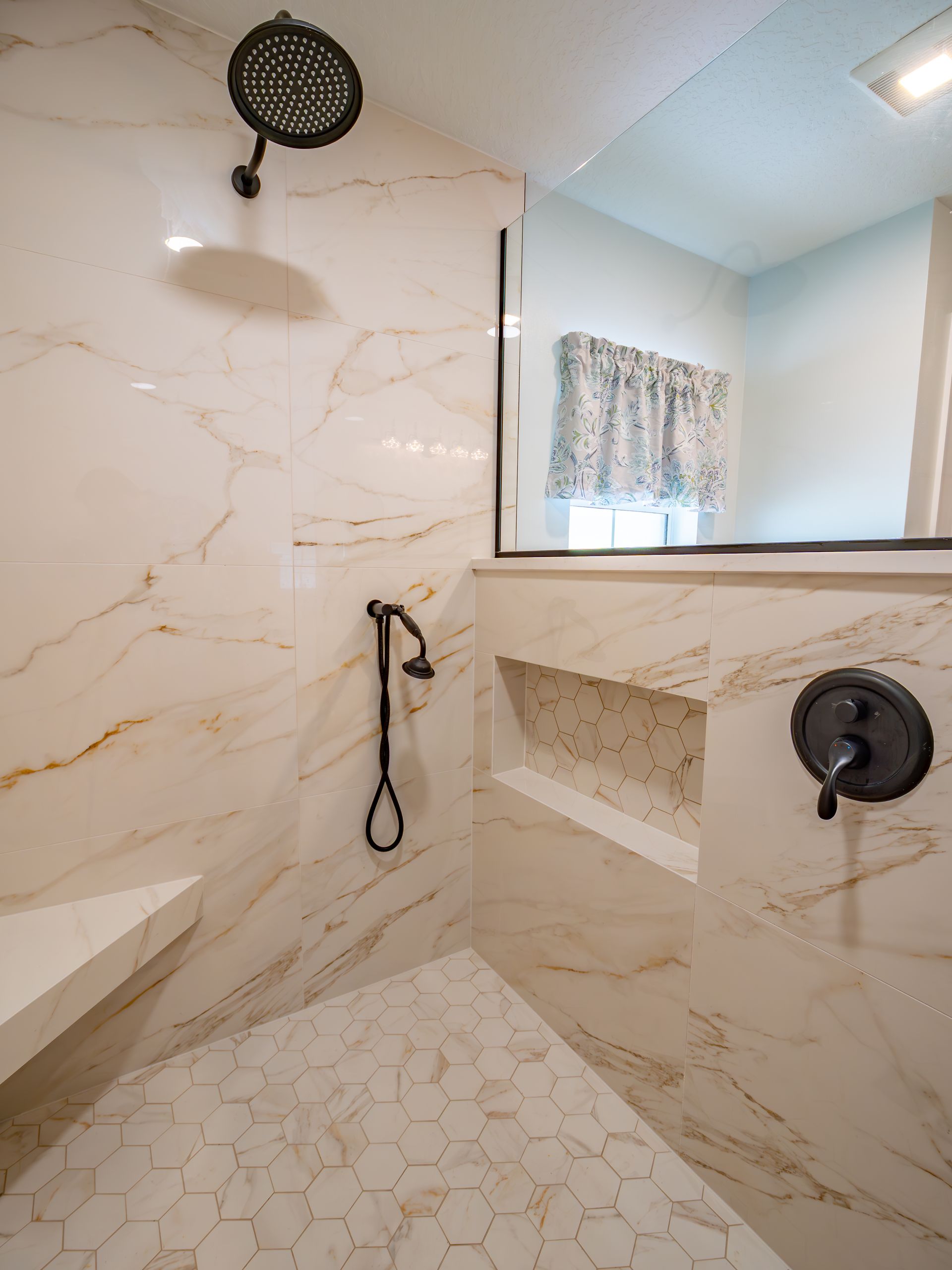 A marble-tiled shower with a black showerhead and fixtures, including a built-in bench and shelves.