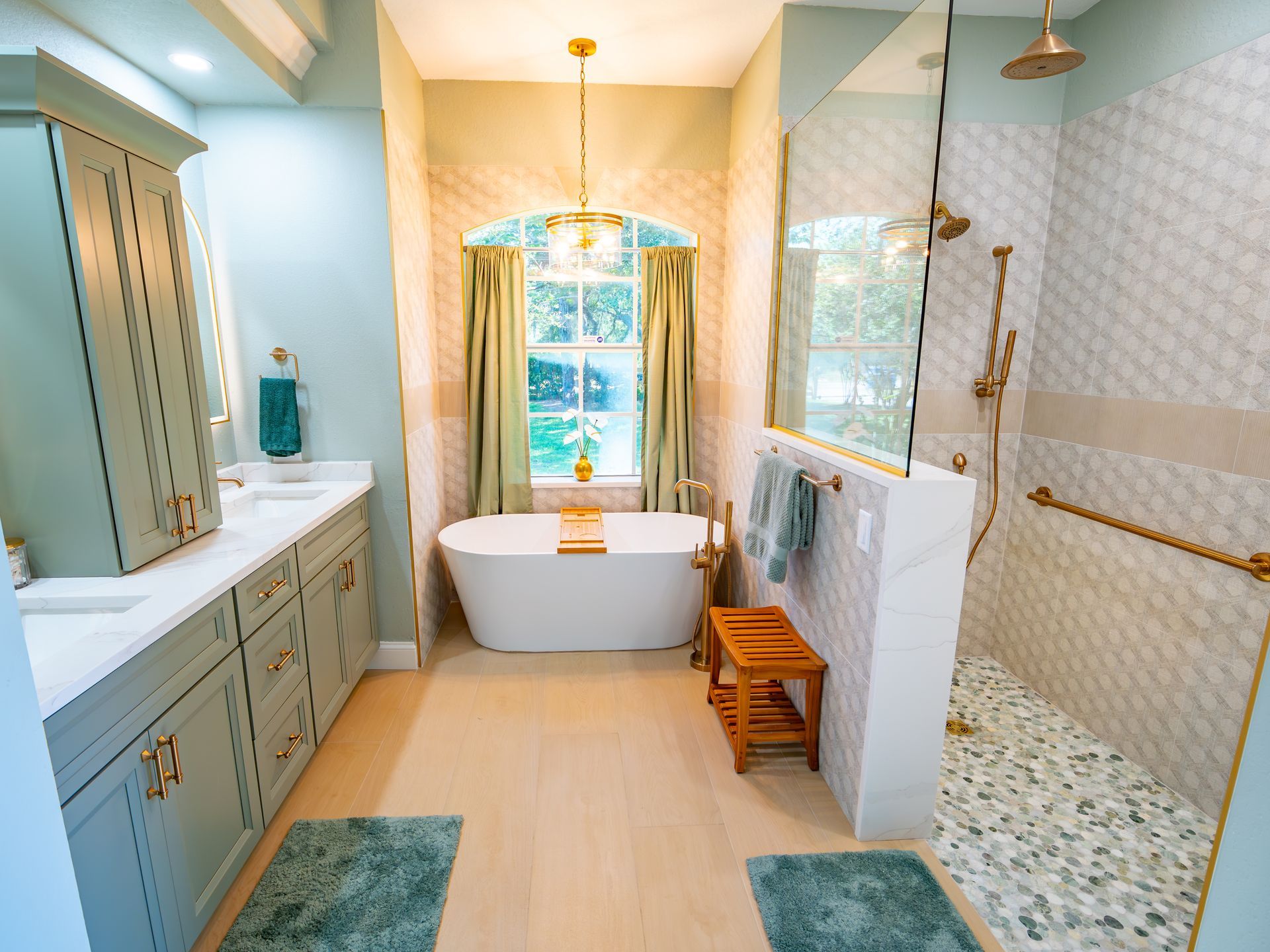Spacious bathroom with a freestanding tub, walk-in shower, and green cabinetry; light blue walls and gold fixtures.