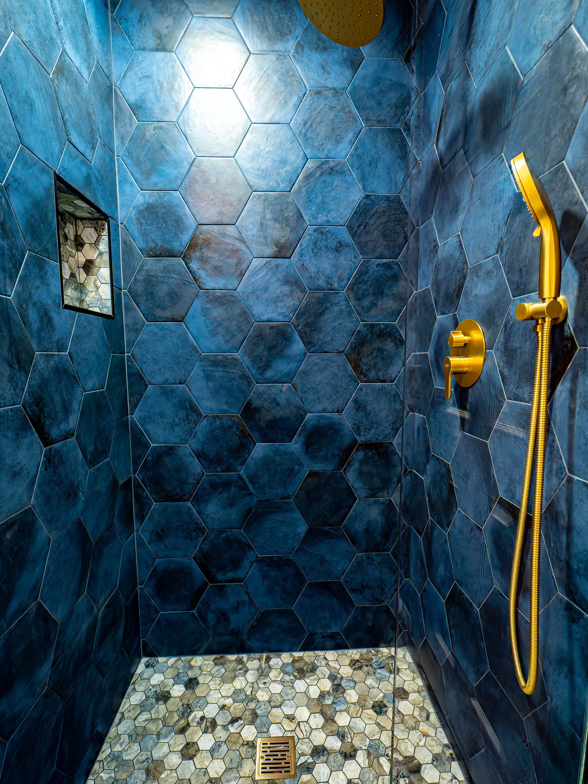 Blue hexagon tiled shower with gold fixtures and pebble floor.