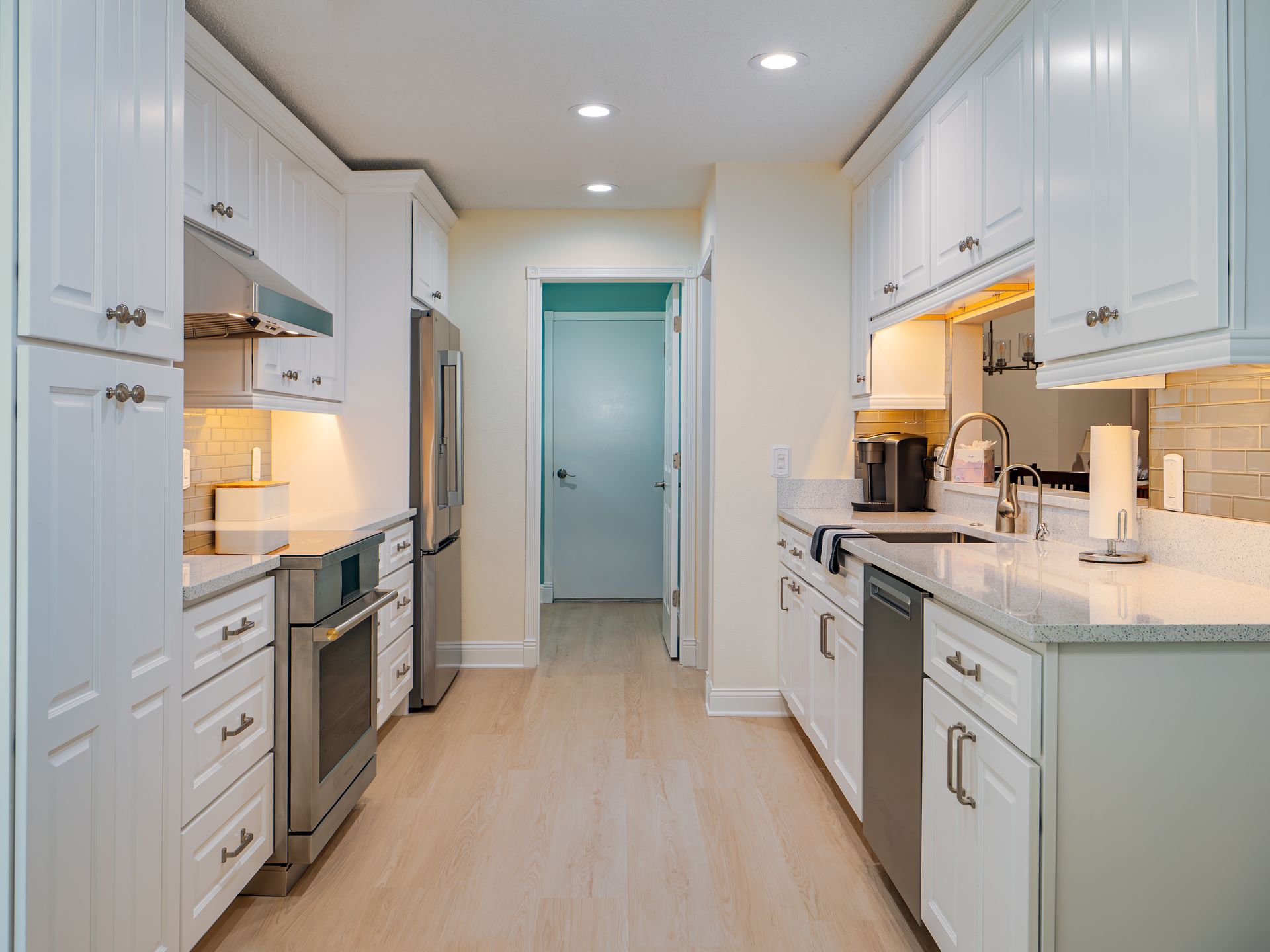 White kitchen with stainless steel appliances and light wood floors.