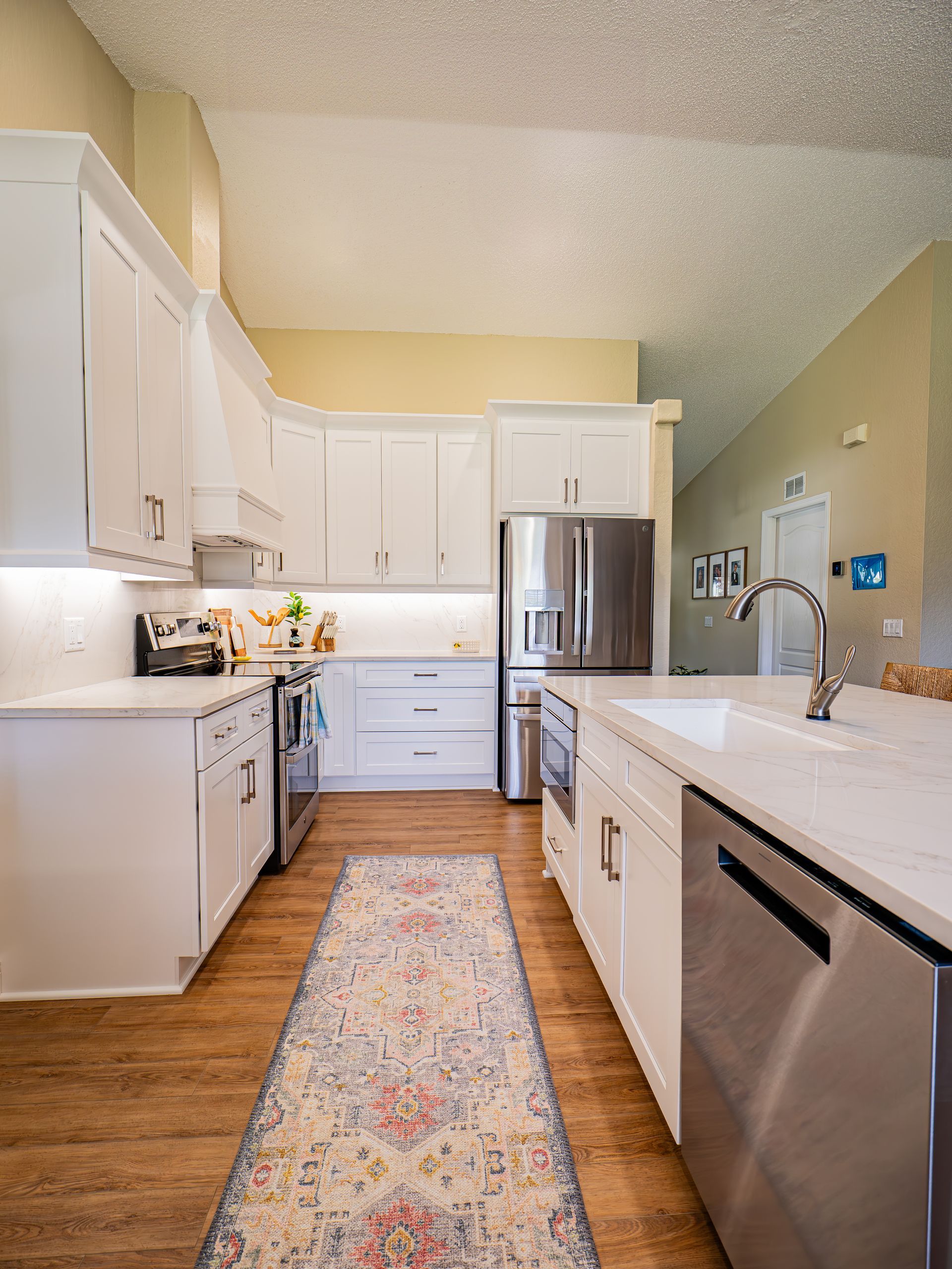 White kitchen with stainless steel appliances, light wood floors, and a patterned rug.